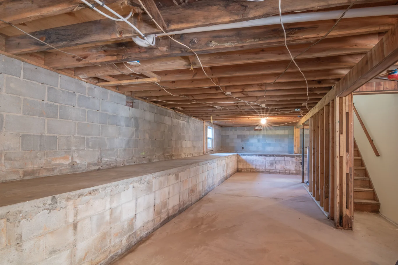 Unfinished basement corridor with exposed pipes and concrete block walls