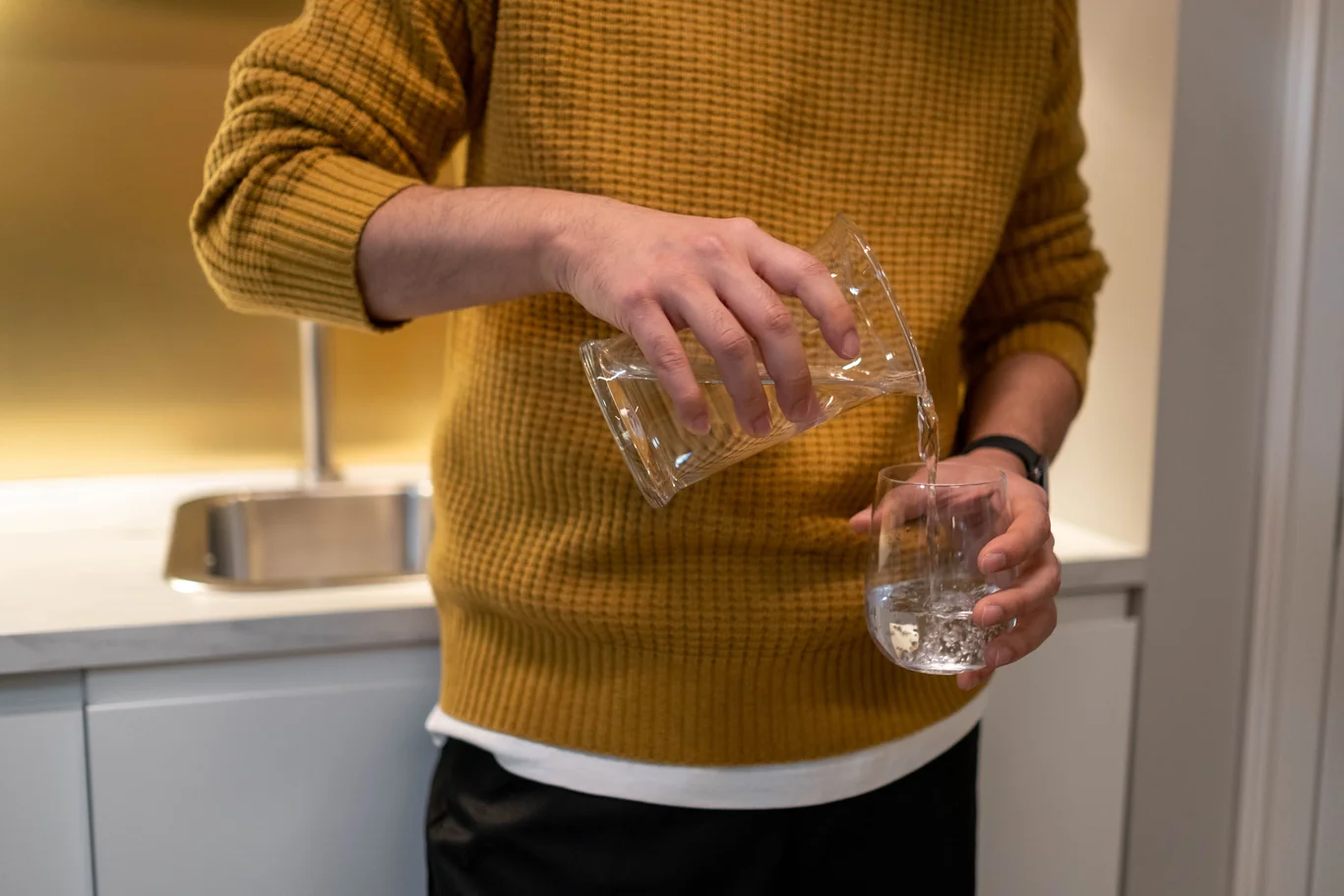 Man pouring filtered water from a jug into a glass beside a kitchen sink