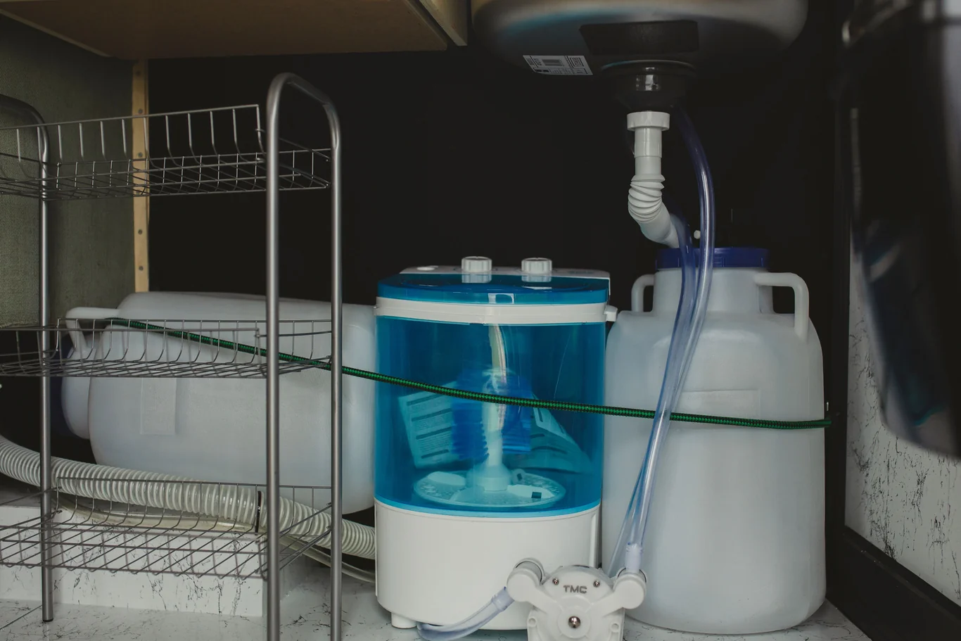 A water filtration tank tucked into a cluttered under-sink cabinet