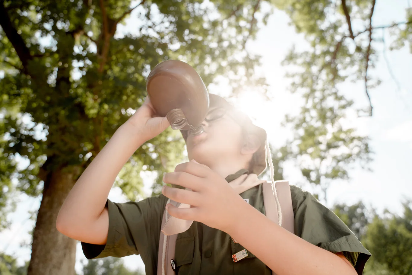 Person using a portable water filter outdoors near trees