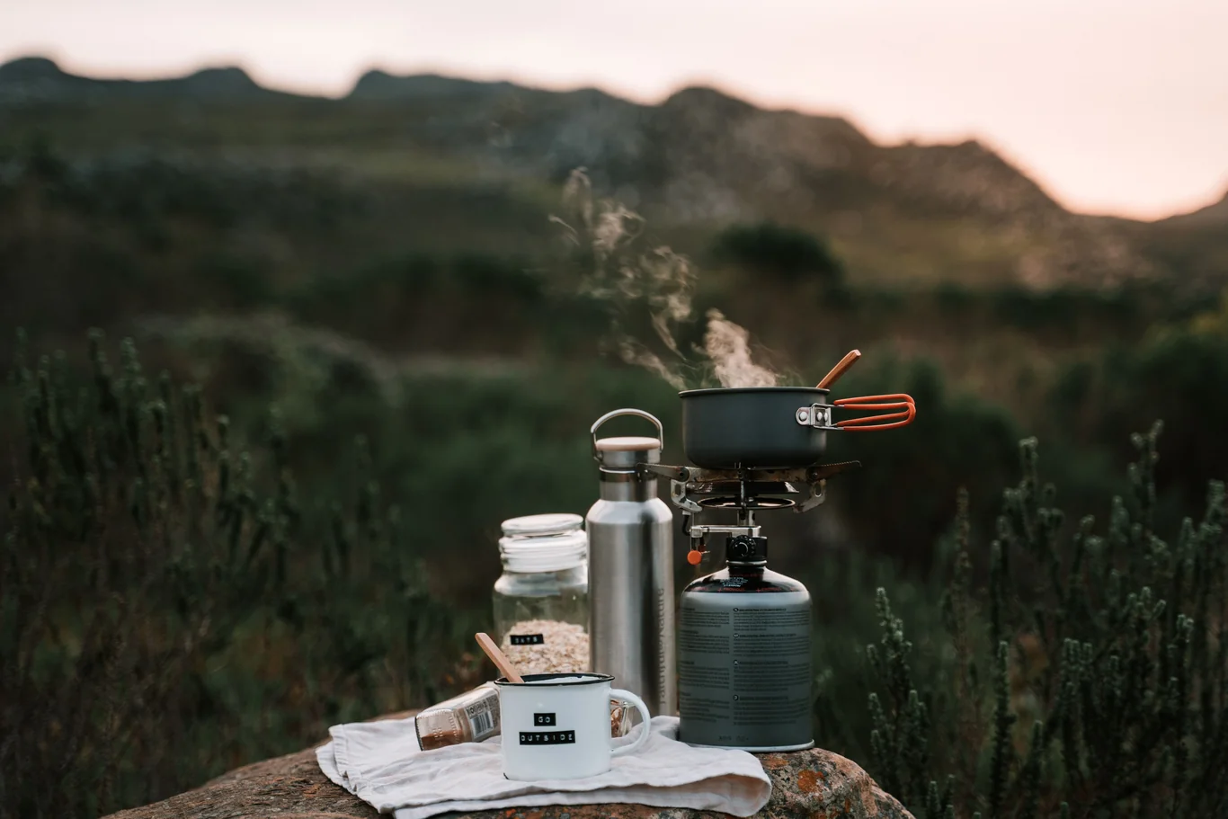Steam rising from a pot heating on a portable camp stove outdoors