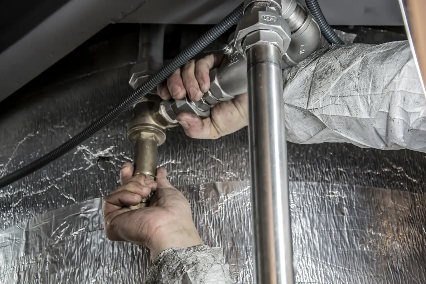 Hands working on plumbing fittings under a kitchen sink during installation