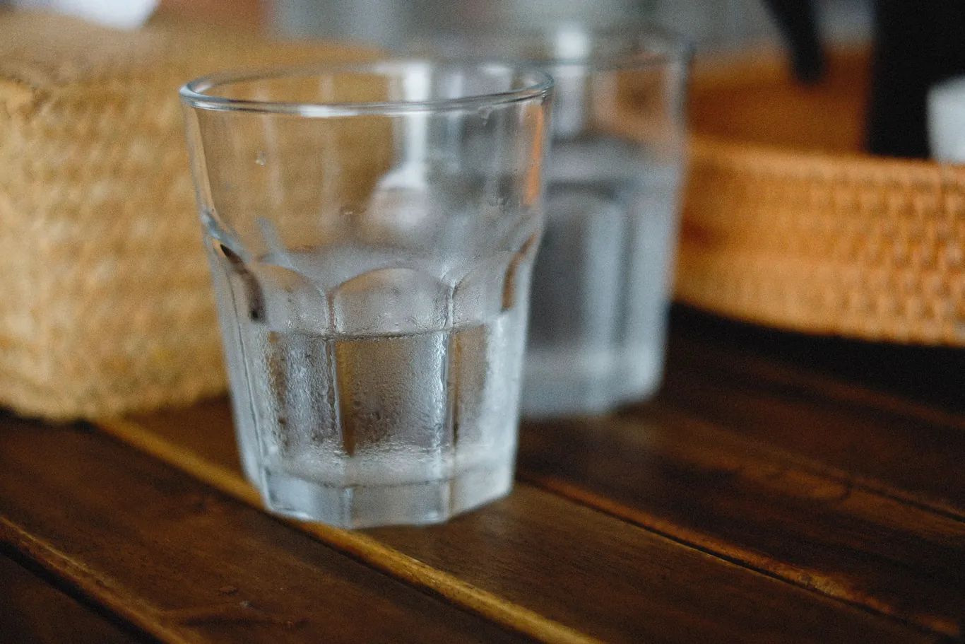 Glass of water beaded with condensation sitting on a sunlit wooden table