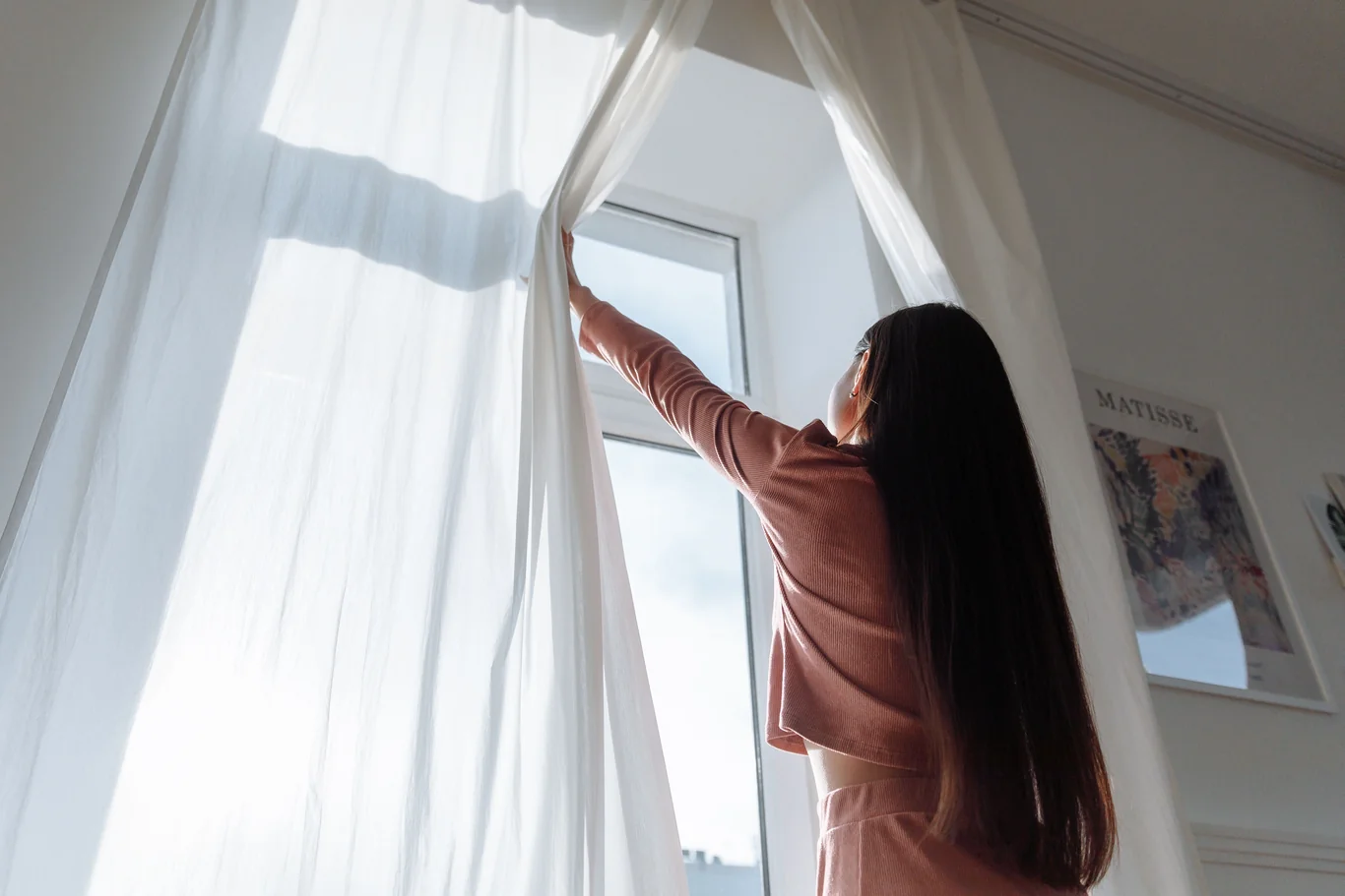 A person opening a window with curtains blowing for fresh air ventilation